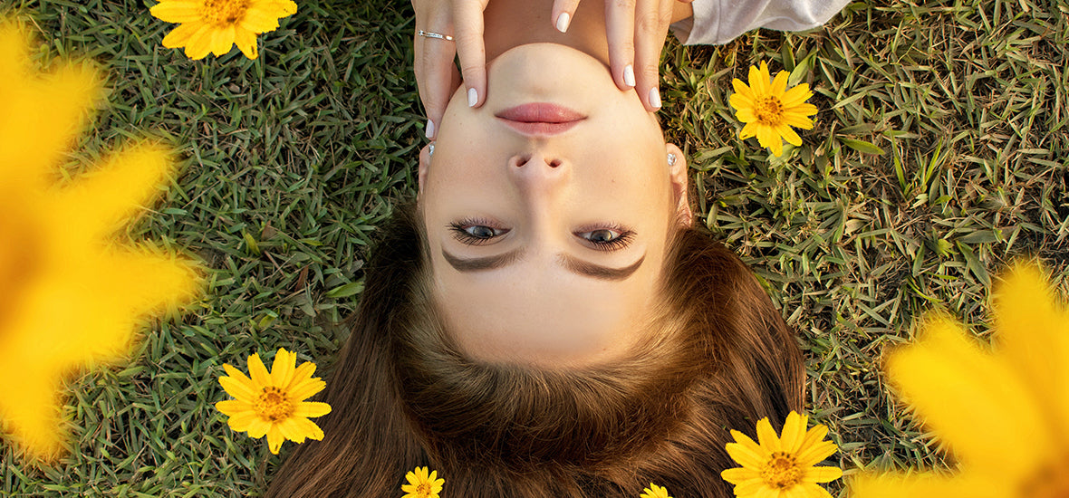 Woman lying on grass with yellow flowers in her brown hair, thinking when to start taking collagen.