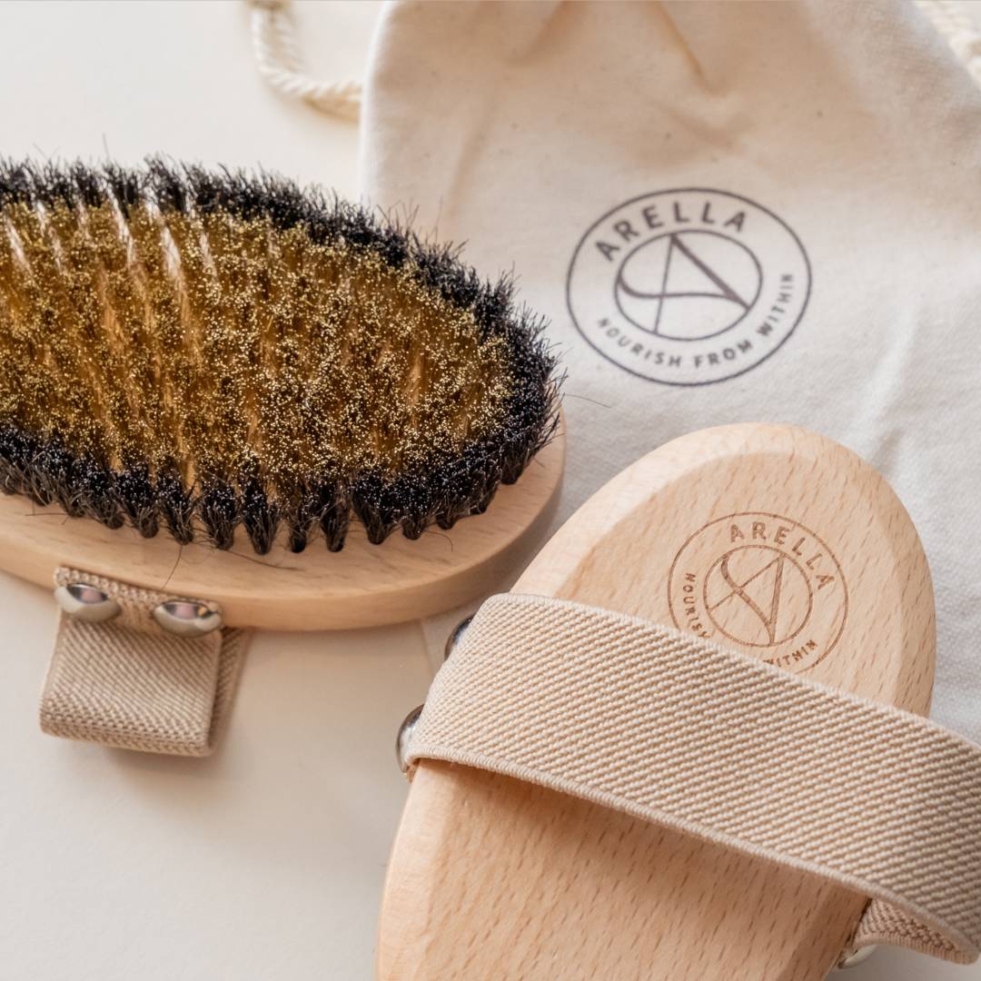 Front and back of the Arella copper body brush beside its branded storage pouch